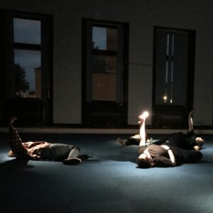 A performance by hidden route. People lying done in a darkened room, holding torches