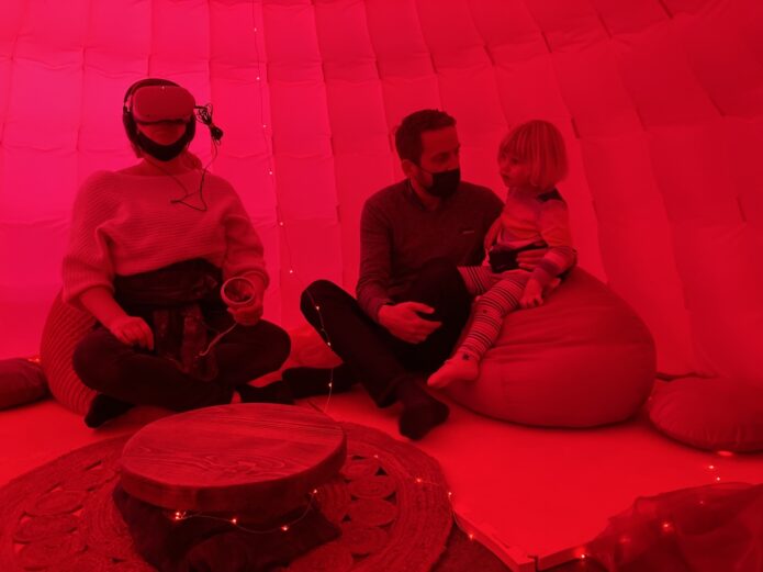INTER_her by Camille Baker. Audience sitting on bean bags, in red light. One audience member wearing VR.
