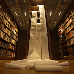 Three rolls of blank paper being unfurled in a dark library full of books.