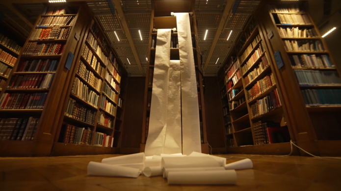 Three rolls of blank paper being unfurled in a dark library full of books.