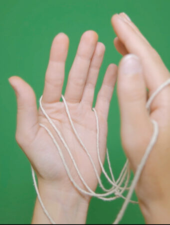 Hands holding twine, hands are open and in front of a green background. Image by Siri Black.