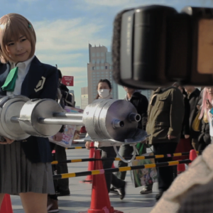 A Japanese schoolgirl holding a large , futuristic looking gun while a group of people look on.
