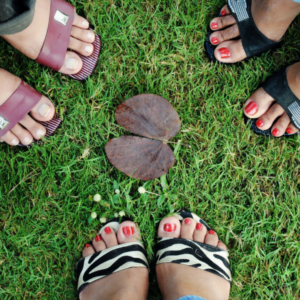 An aerial view of three pairs of feet, all wearing open toed sandals, standing on a patch of grass.