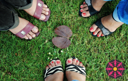 An aerial view of three pairs of feet, all wearing open toed sandals, standing on a patch of grass.