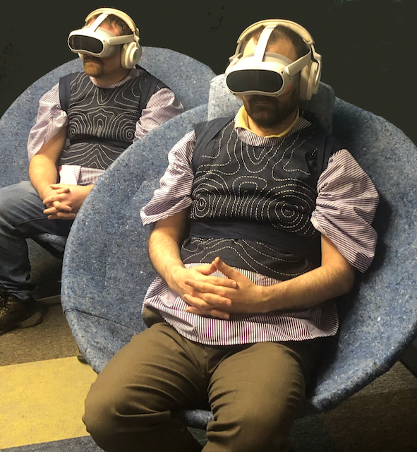 Two people sitting in chairs with VR headsets on. 